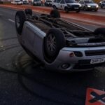 Cena de acidente com carro capotado em avenida de Brasília, viaturas da PMDF no local, representando embriaguez ao volante e perda de habilitação.
