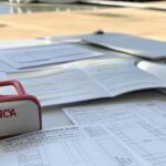 Edifício da CLDF em Brasília com papéis de concursos e kit de primeiros socorros, destacando obrigatoriedade que complica candidatos no DF.