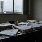 Edifício da CLDF em Brasília com documentos espalhados, representando atrasos em lei contra supremacismo no DF.