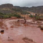 Paisagem devastada por tragédia ambiental na Zona da Mata Mineira, com florestas destruídas e rios transbordando.