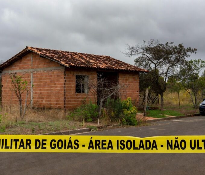 Casa em Águas Lindas de Goiás isolada por fita policial, viatura da PM ao lado, representando cena de tragédia familiar.