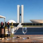 Garrafas de vinhos exclusivos da Vinícola Brasília com arquitetura da capital ao fundo, celebrando 2 anos e 66 anos de Brasília.